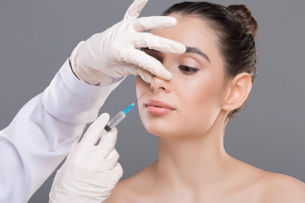 Woman receiving dermal filler injections into the tip of her nose for subtle enhancement