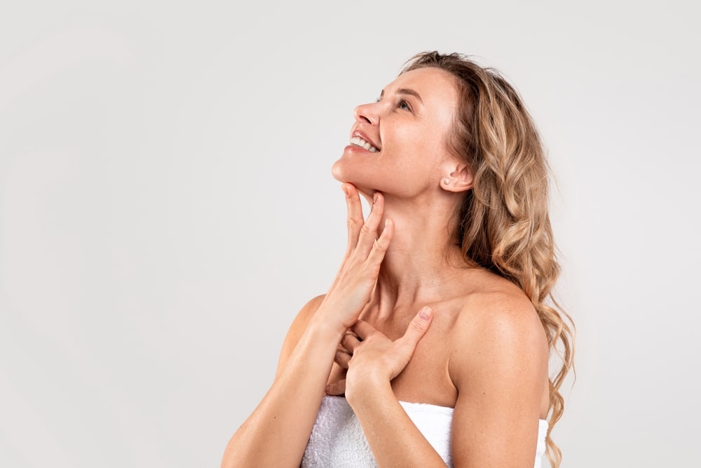Profile of woman touching her sharp, defined jawline after Kybella injections.