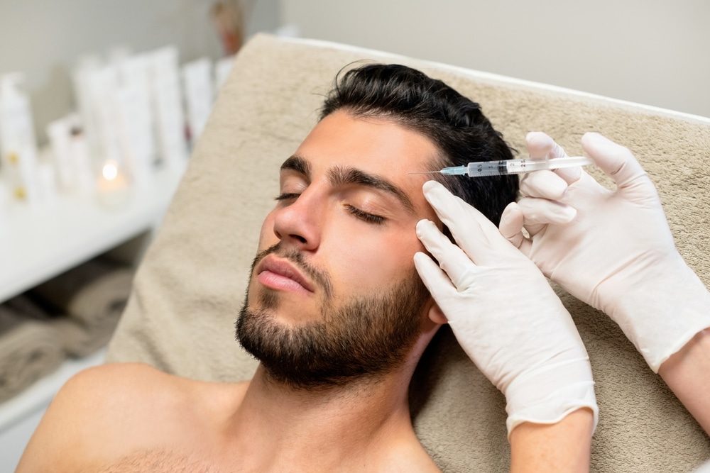 Bearded young man receiving Botox injections to his forehead to reduce wrinkles and signs of aging.