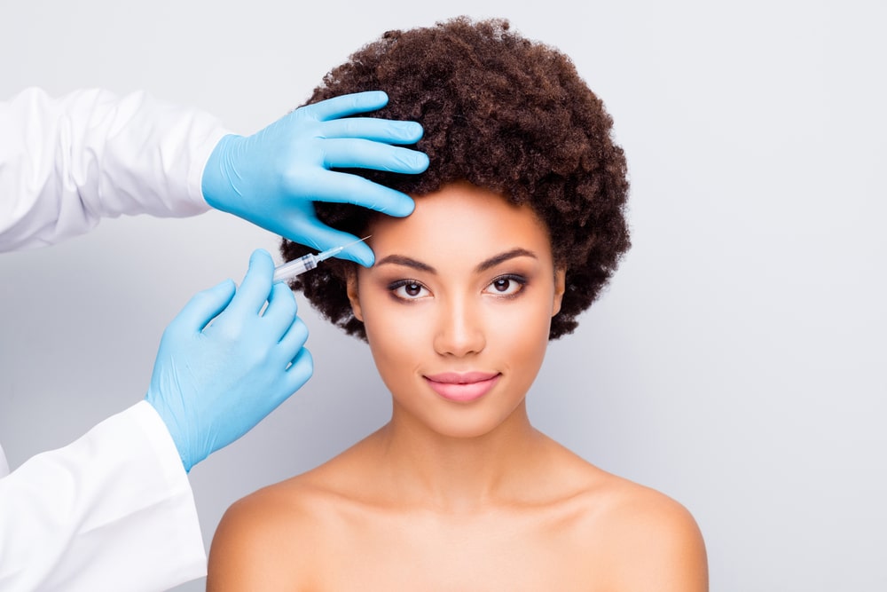 Beautiful young black woman receiving Botox injections to her forehead for subtle, natural refinement.