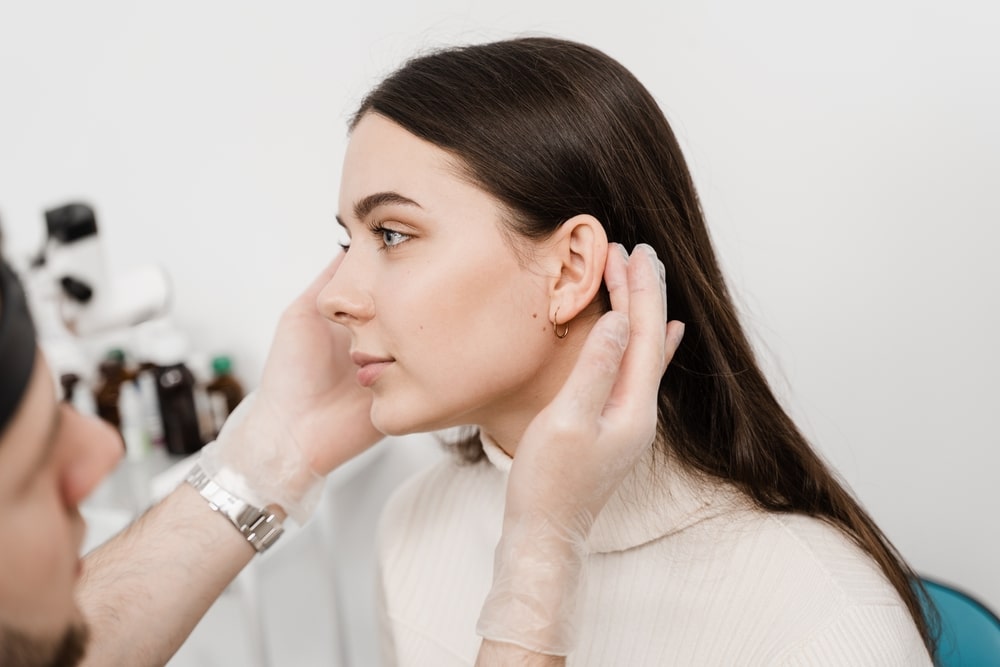 Young woman having her ears examined by her plastic surgeon before an otoplasy, or ear shaping, procedure.