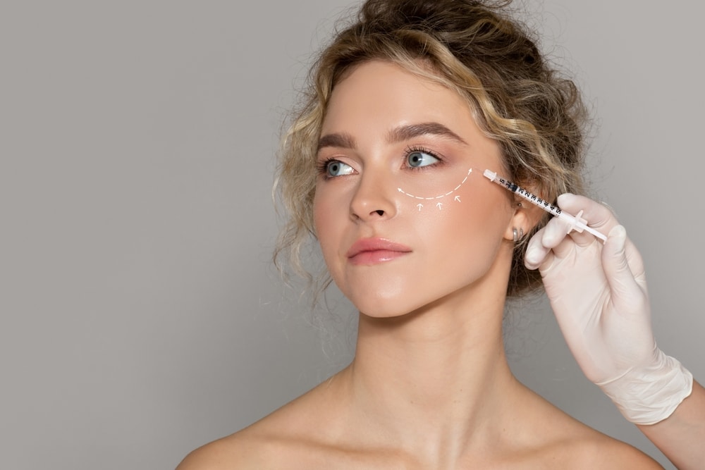Young woman receiving filler injections to her under eye to help restore facial volume loss.