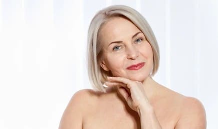 Older woman smiling and touching her face after getting a deep-plane facelift to reduce signs of aging.